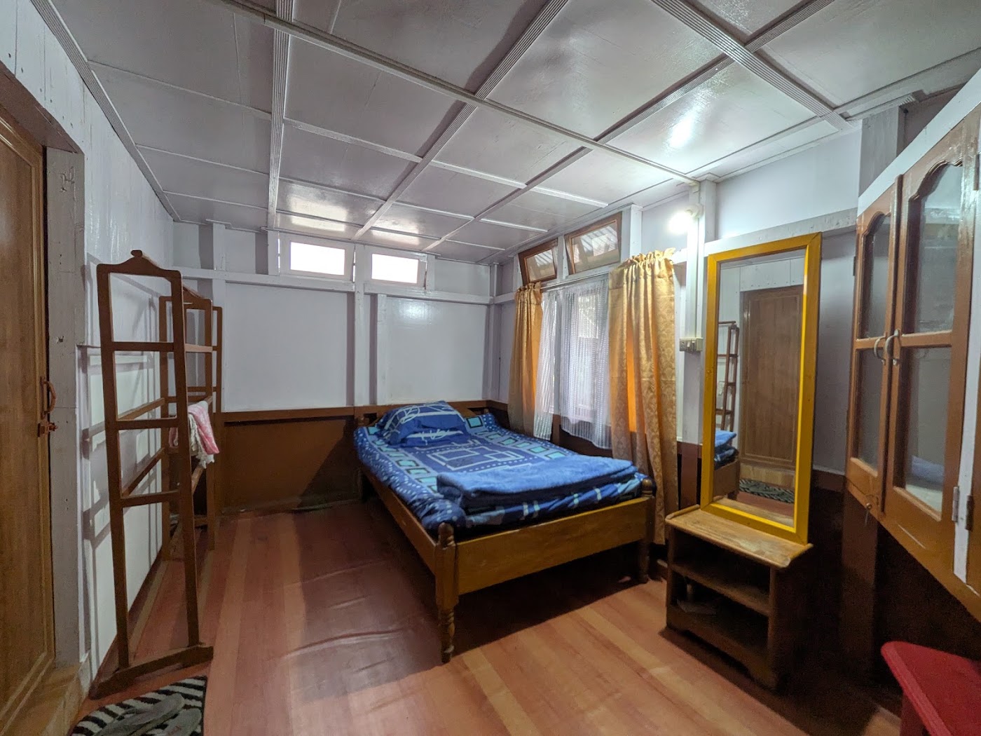 A single wooden bed with a blue cover, a wardrobe, and a yellow-framed mirror