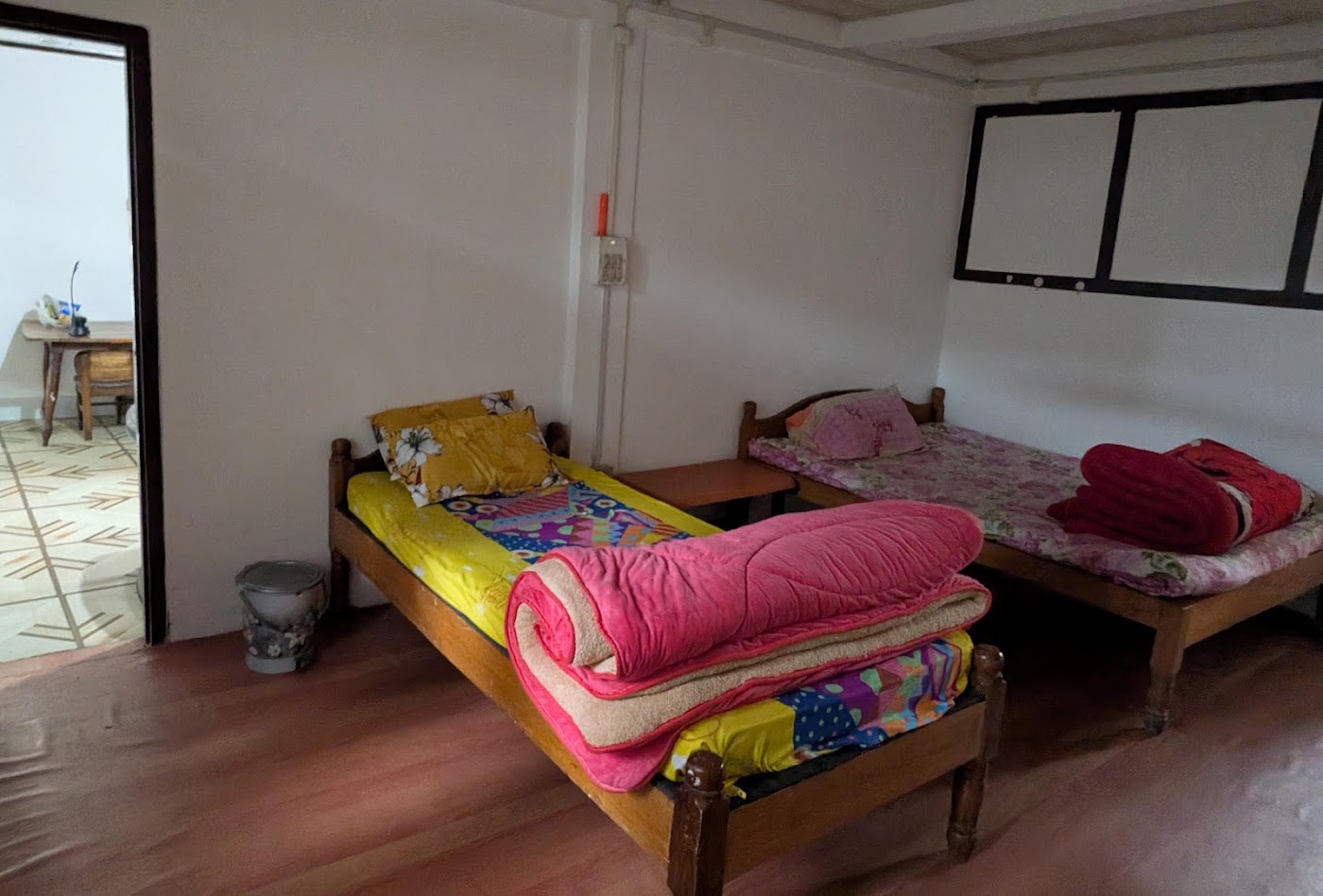 Two wooden single beds in a white room, one with a yellow cover and one with a floral cover
