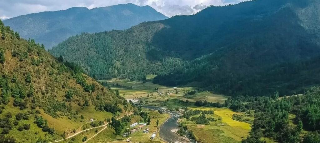A river bending through rice fields, with forested ridges closing the valley on both sides