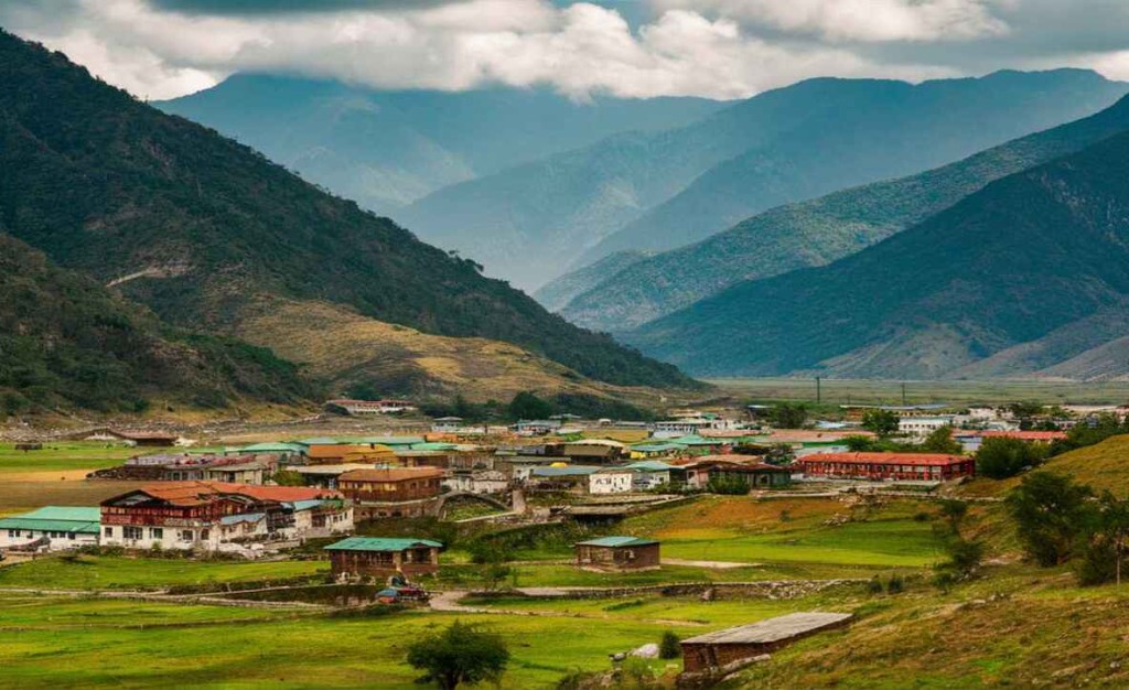 A village of metal and timber roofs on the green floor of Ziro, with cloud on the ridges behind